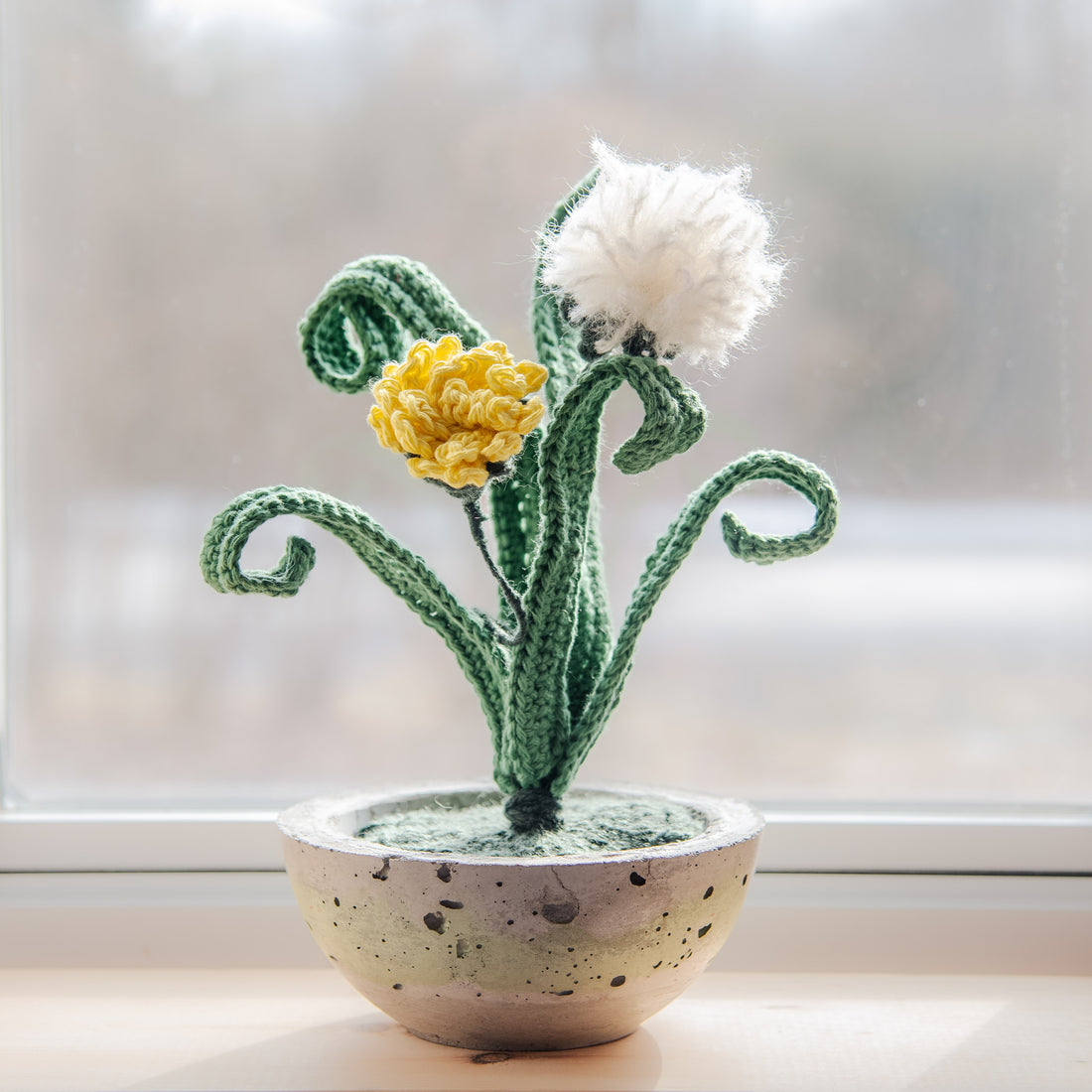 Pissenlit en crochet dans un pot en béton, une touche écoresponsable en laine naturelle.